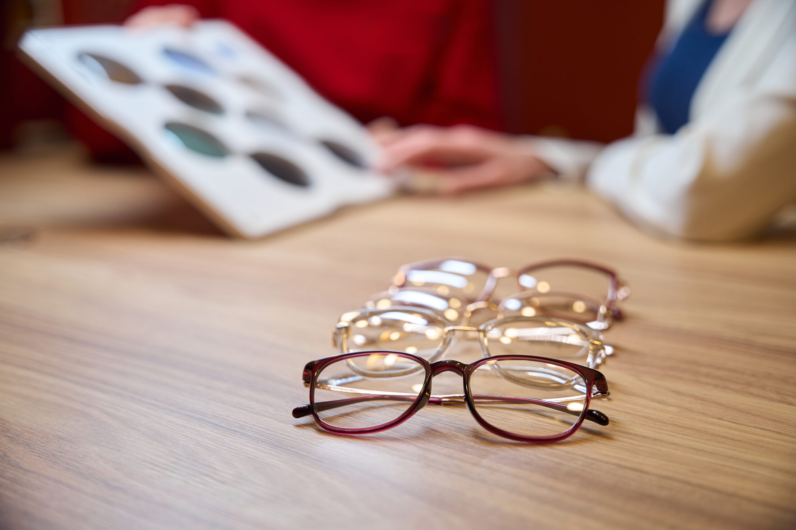Stylish glasses with different frames lie on the table, two women are talking at the table